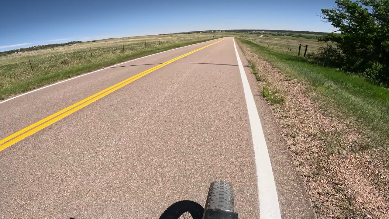 A two-lane rural road from the bike, with fields on both sides.
