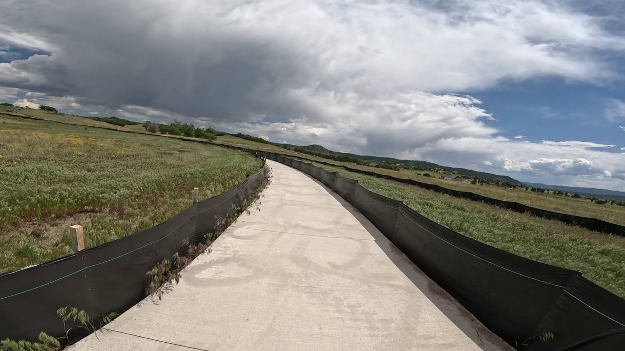 A concrete path through open fields under a stormy sky.